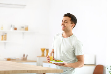 Young man holding tasty sandwich and glass of juice in kitchen