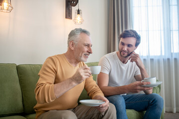 Father and son sitting next to each other and drinking tea