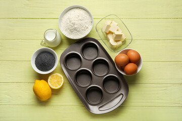 Baking tin and ingredients for delicious muffins with poppy seeds on color wooden table