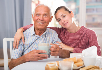 Elderly father and adult daughter talk and drink tea in the kitchen. High quality photo