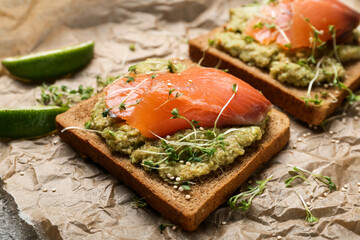 Tasty sandwiches with guacamole and salmon in parchment on table, closeup