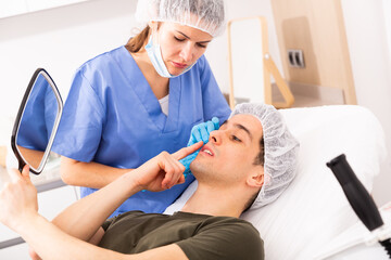 Confident woman cosmetologist examining male client face before procedure in esthetic clinic