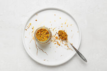 Jar and spoon with bee pollen on light background