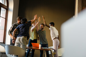 Fototapeta na wymiar Casual business people raising hands in circle in sunny office meeting