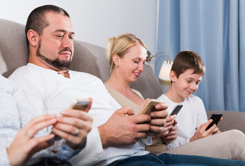 Parents and teen son using phones sitting on sofa at home