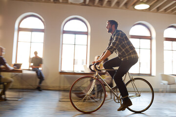 Casual businessman riding bicycle in open office