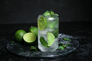 Glass of fresh mojito and limes on dark background