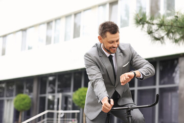 Businessman with bicycle looking at wrist watch on city street