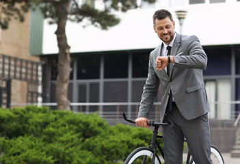 Businessman with bicycle looking at wrist watch on city street