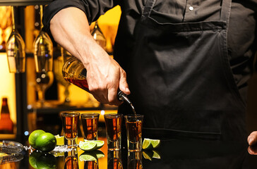 Bartender pouring tasty tequila into glasses at table in bar, closeup