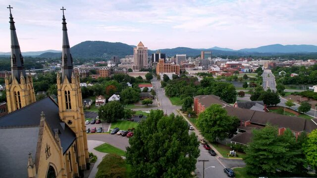 aerial push over roman catholic church with roanoke virginia skyline in background