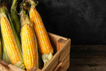 Box with fresh corn cobs on wooden table