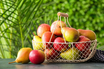 Basket with ripe pears and apples on table outdoors