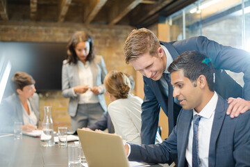 Businessmen using laptop in conference room