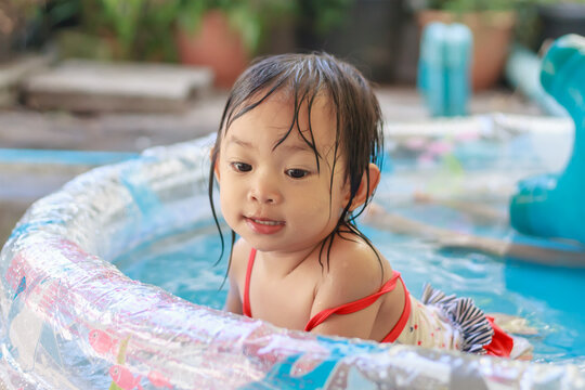 Portrait image of 3-4 years old baby. Happy Asian child girl swimming and play water in the blue pool. She smile and laugh. Summer season.