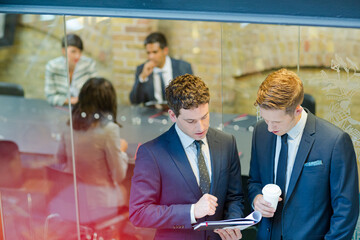 Businessmen discussing paperwork outside conference room meeting