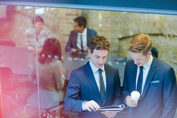 Businessmen discussing paperwork outside conference room meeting