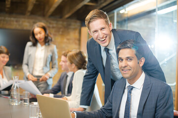 Businessmen smiling at laptop in conference room meeting