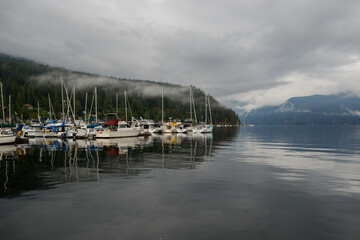 Fototapeta premium The anchor yacht in harbor After rain cloudy sky, misty forest mountains and calm water.