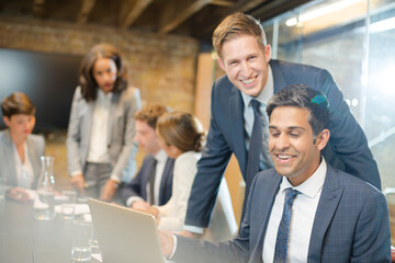 Businessmen smiling at laptop in conference room meeting