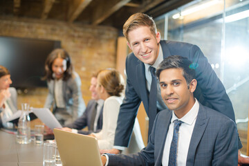 Businessmen smiling at laptop in conference room meeting