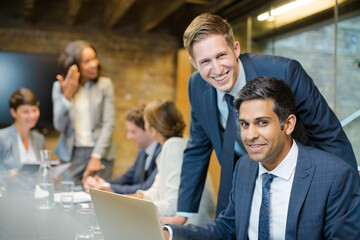 Businessmen smiling at laptop in conference room meeting