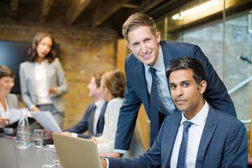 Businessmen smiling at laptop in conference room meeting