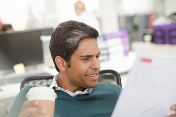 Smiling businessman drinking coffee and reviewing paperwork