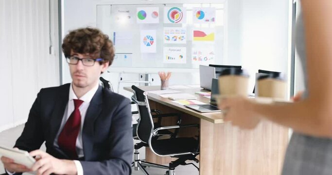 Businessman sitting and working in concentrate and focus at desk while businesswoman buddy colleague brings cups of coffee walking to him with care and concern. Good team and friendship idea.
