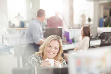 Portrait smiling fashion designer drinking coffee at computer in office