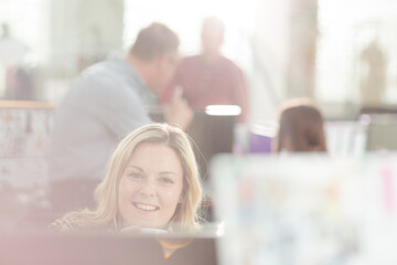 Portrait smiling fashion designer drinking coffee at computer in office