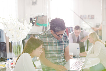 Obraz premium Smiling fashion designers working at laptop in office