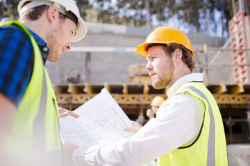 Construction worker engineer reviewing blueprints below crane at construction site