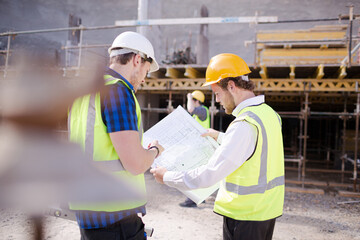 Construction worker engineer reviewing blueprints below crane at construction site