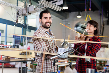Cheerful positive smiling team of aircraft enthusiasts holding sports airplane models in workshop