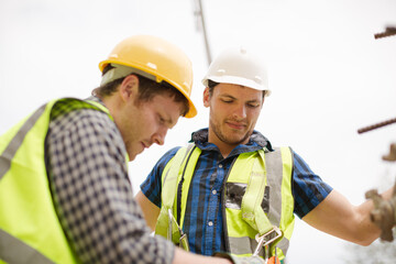 Construction worker fastening coworker‚Äö√Ñ√¥s safety harness