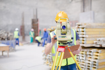 Engineer with clipboard using theodolite at construction site