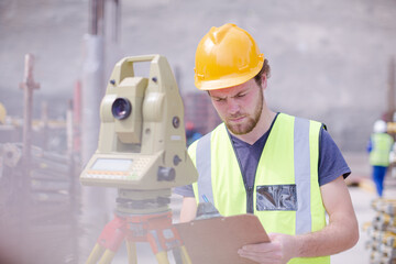 Engineer with clipboard using theodolite at construction site