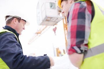 Foreman talking to construction worker below crane at construction site