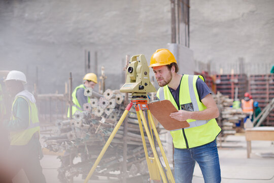 Engineer with clipboard using theodolite at construction site