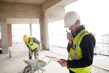 Foreman with digital tablet using walkie-talkie at construction site