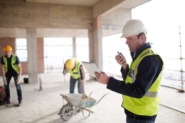 Foreman with digital tablet using walkie-talkie at construction site