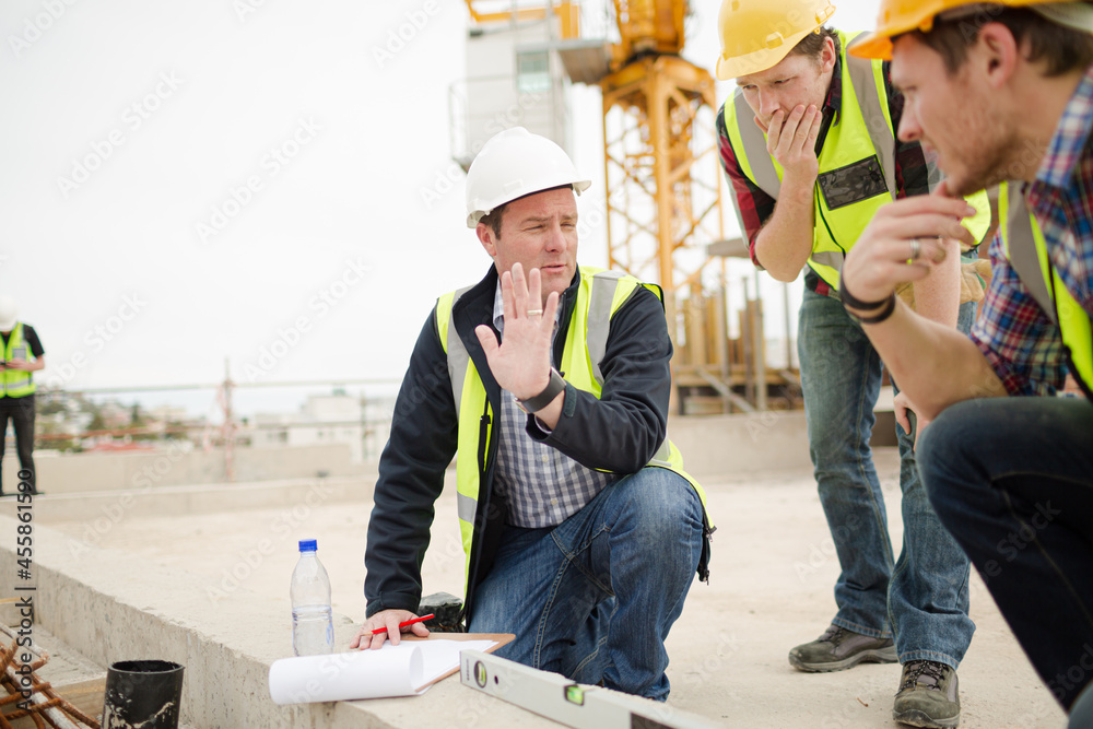 Wall mural Construction workers using level tool below crane at construction site