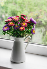 Bouquet of bright multicolored autumn flowers asters on the window sill in a bright room