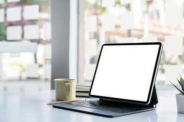 Blank screen tablet with magic keyboard on white top table in modern office room.