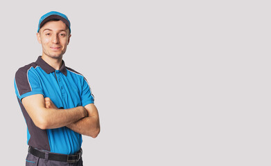 Delivery man having joyful face expression wearing blue postman uniform standing with cross hands, side empty space.