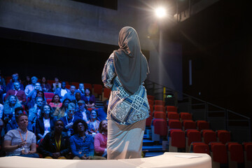 Female speaker in hijab on stage talking to audience