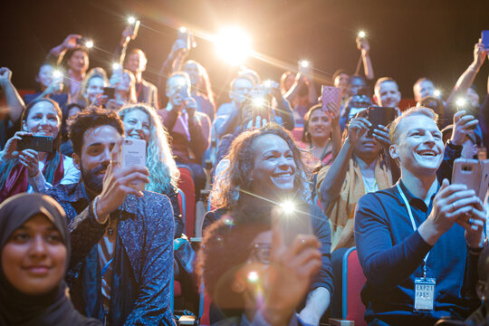 Eager audience with smart phone flashlights in dark auditorium