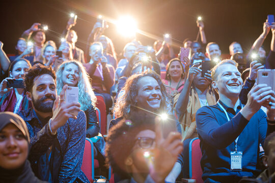 Eager audience with smart phone flashlights in dark auditorium