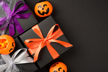 Top view photo of halloween composition three black gift boxes with violet orange and white ribbon bows pumpkin baskets candy corn spiders and web on isolated black background with copyspace